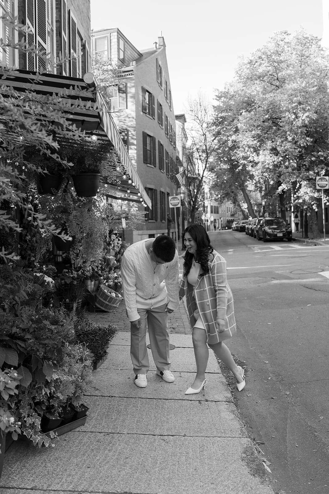 Black-and-white candid of a couple laughing together while walking past a flower shop on Beacon Hill.