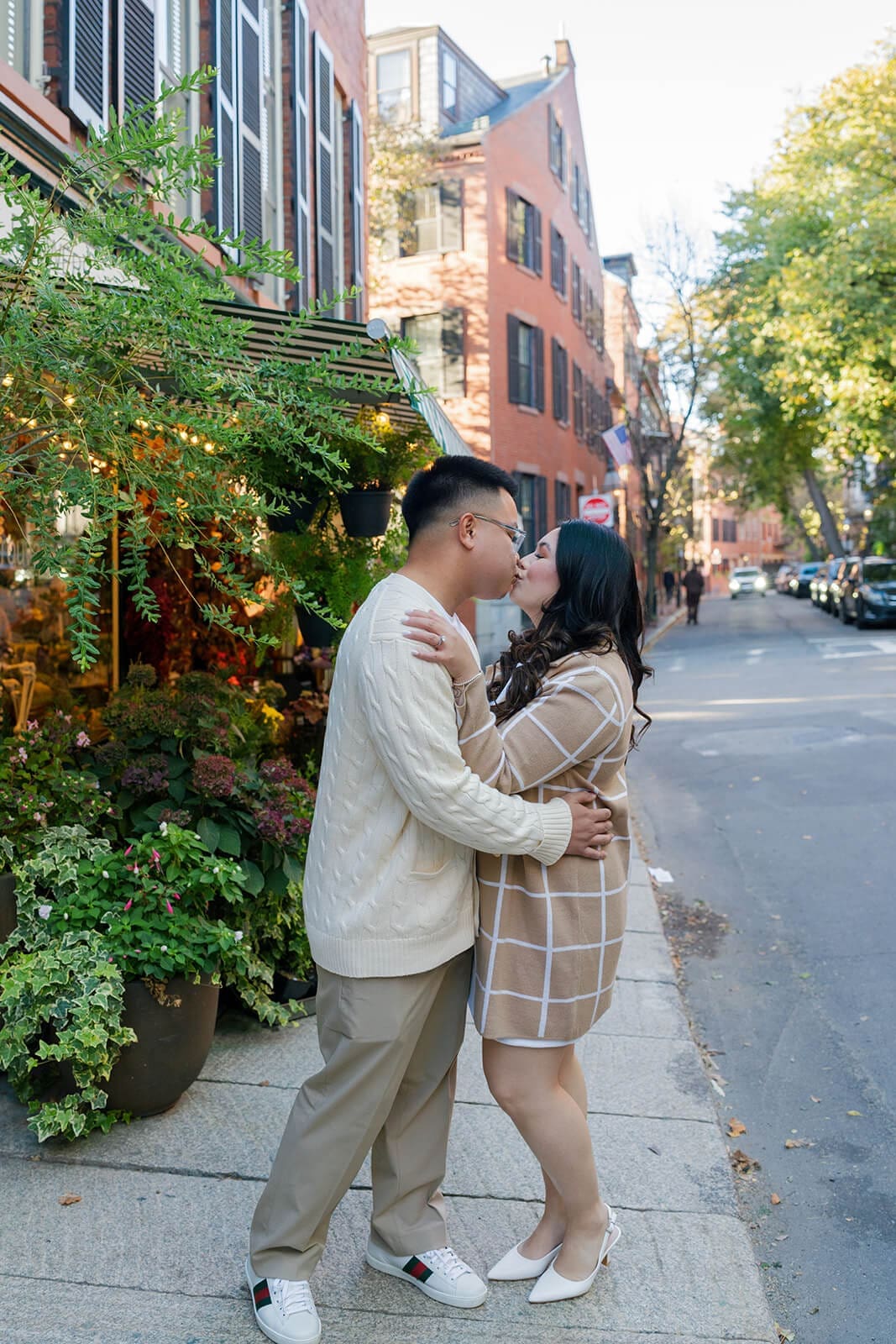 Couple kissing on the sidewalk beside a flower shop on a quiet Beacon Hill street.