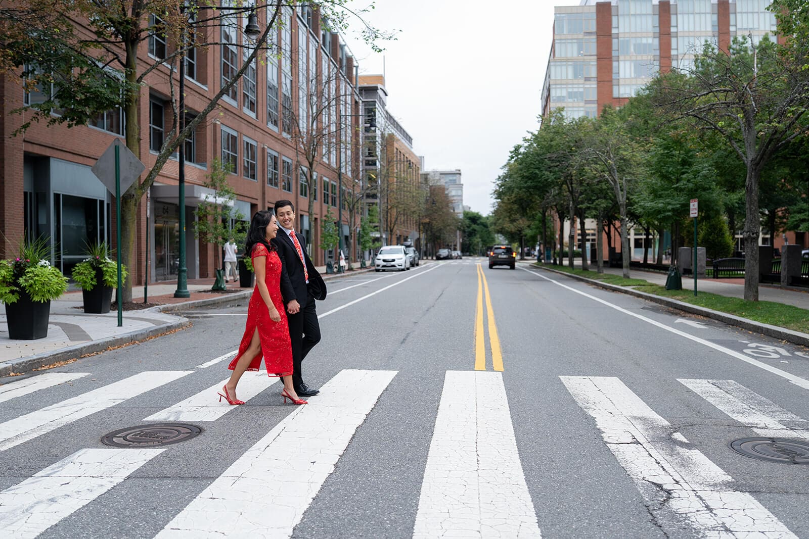 Couple in formal attire crossing a Cambridge city street together during their pagu restaurant wedding portraits.