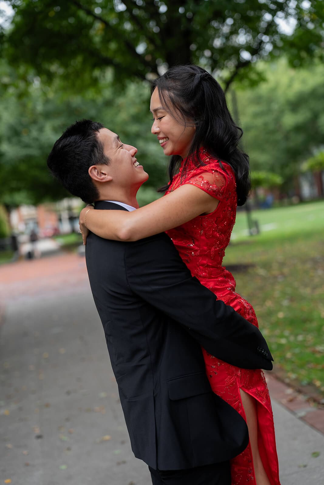Man lifting his partner in her red embroidered dress as they laugh together outdoors.
