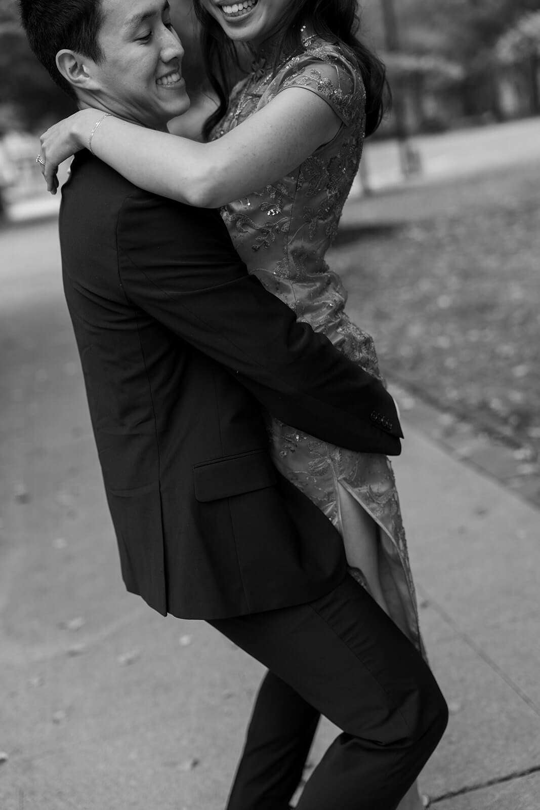 Black-and-white candid of the woman laughing while being lifted into the air by her partner.