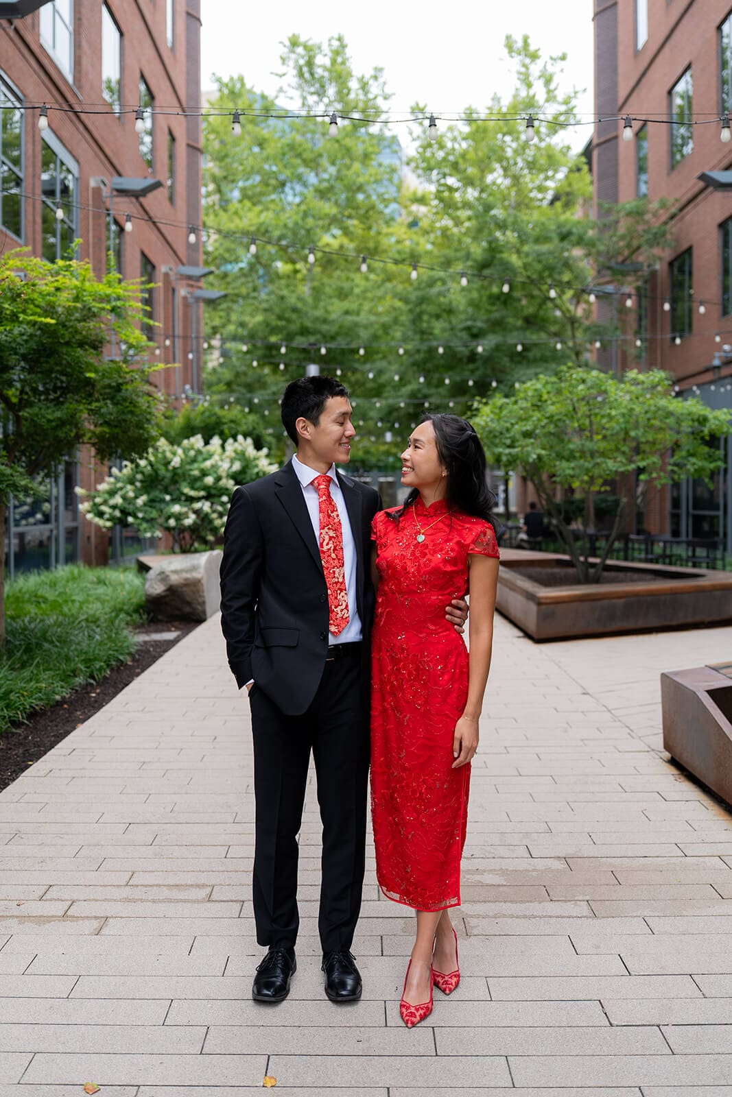 Couple walking together through a courtyard in red and black formal attire during their pagu restaurant wedding portraits.