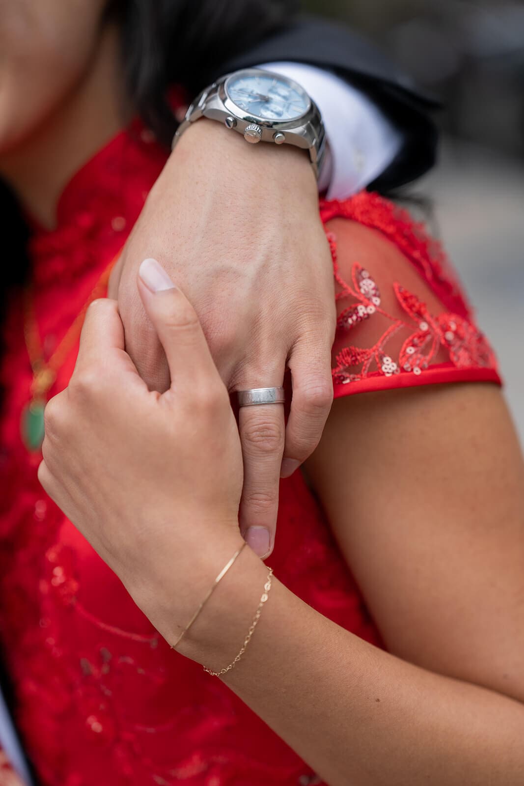 Close-up of the couple's hands and wedding bands against the woman's red dress during their pagu restaurant wedding.