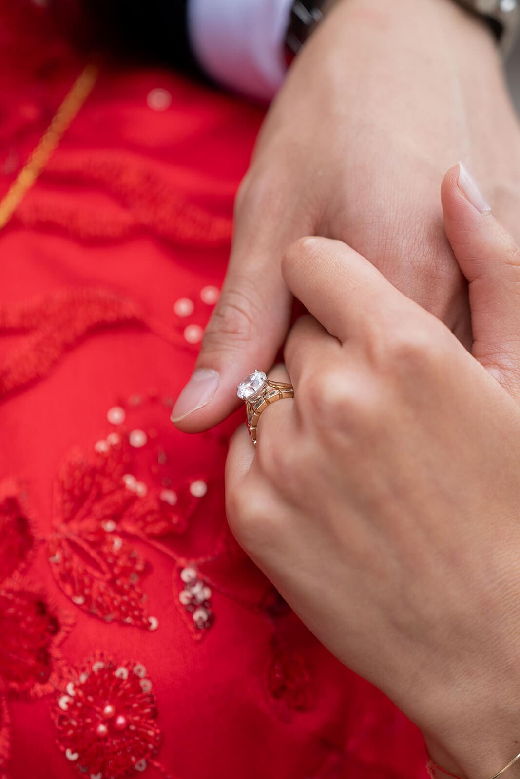 Close-up of the woman's engagement ring and hands resting against the red embroidered fabric of her dress.