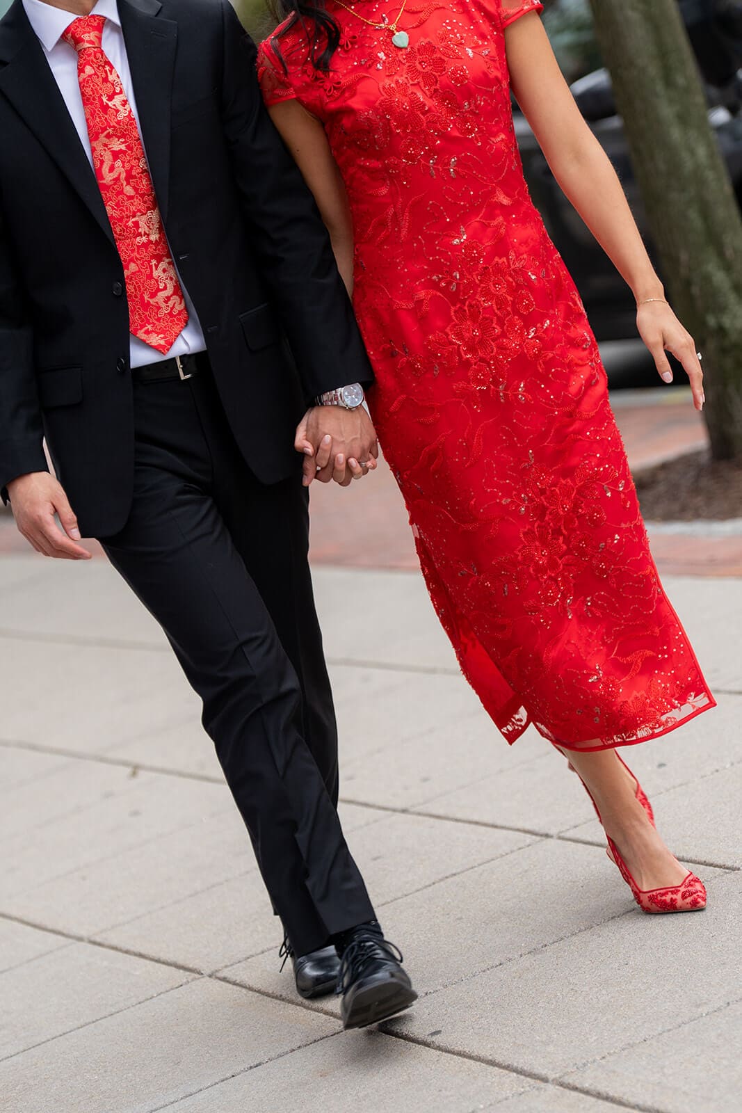 Close-up of the couple holding hands while walking in matching red and black formal attire during their pagu restaurant wedding portraits.