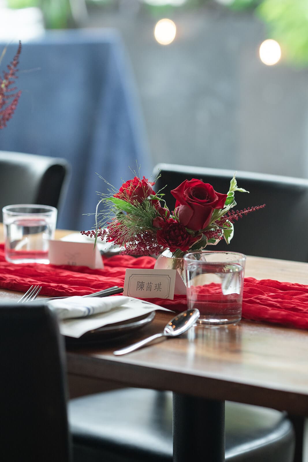 Reception table decorated with a red floral centerpiece, red table runner, place card, glassware, and place setting.