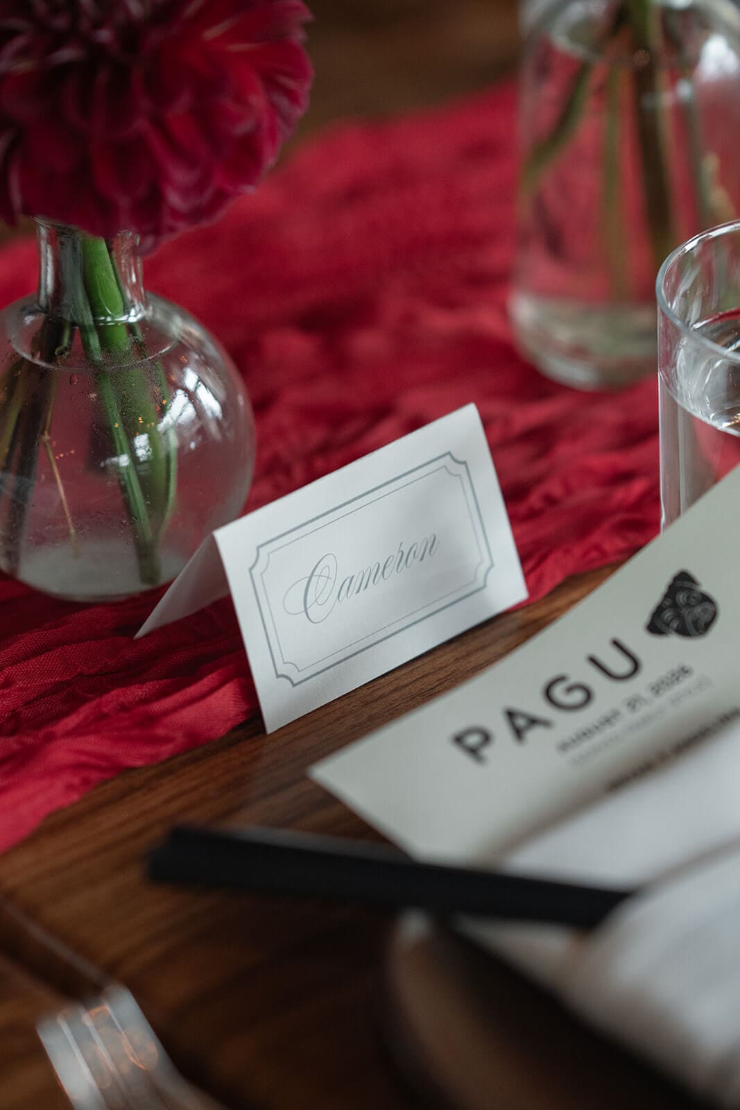 Reception place card beside a small red floral arrangement, red runner, and PAGU menu.
