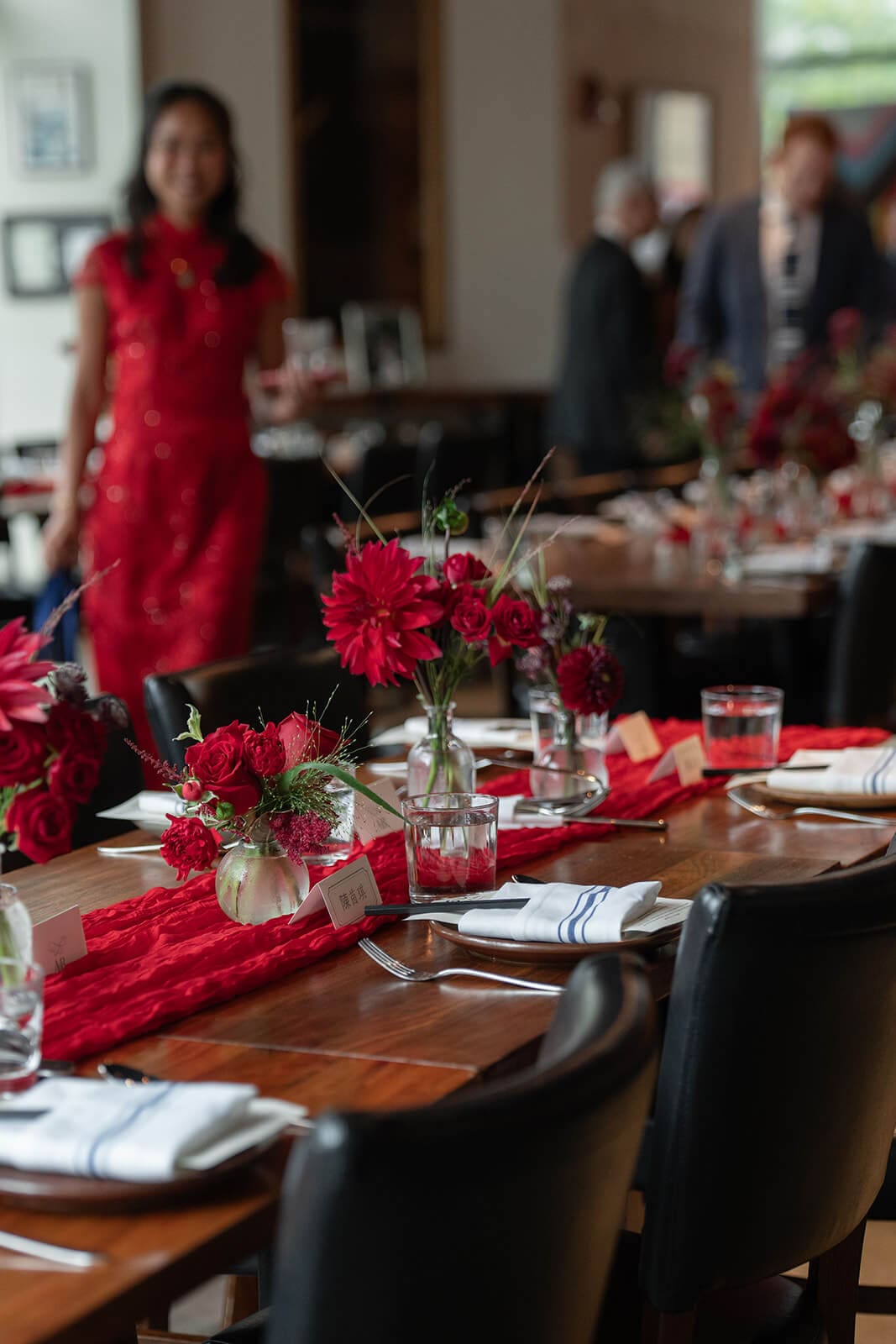 Wooden reception table lined with red floral arrangements, glassware, and place settings during a pagu restaurant wedding.