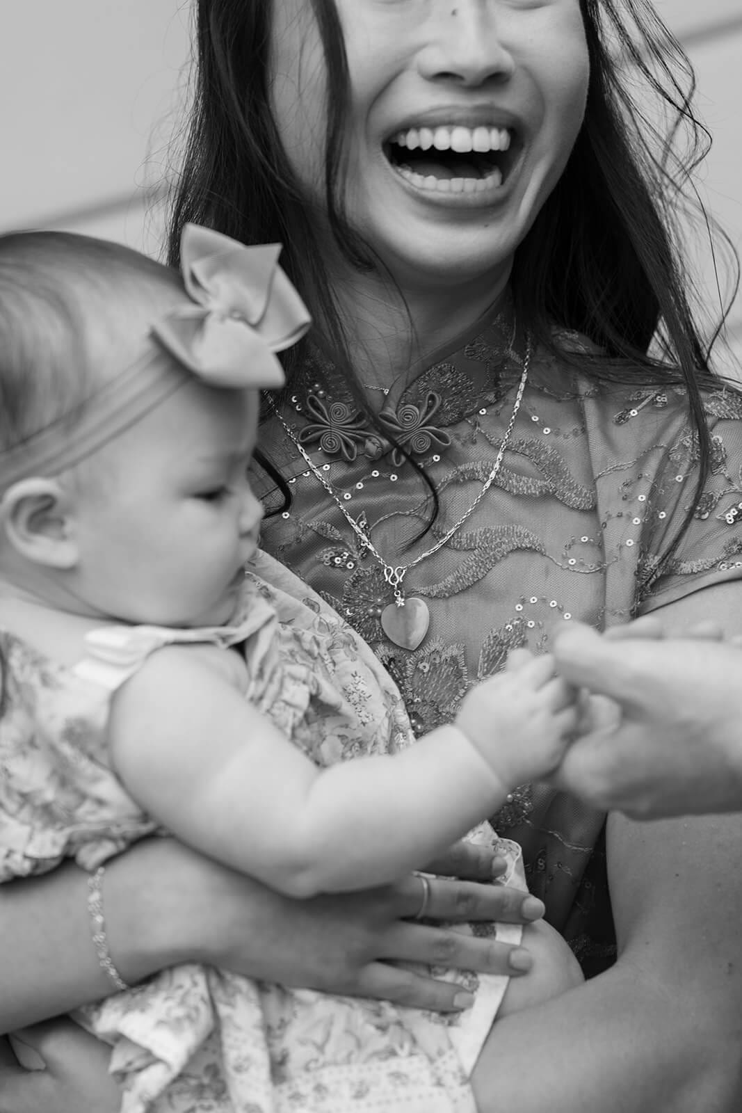Black-and-white candid of a smiling woman holding a baby during a pagu restaurant wedding reception.