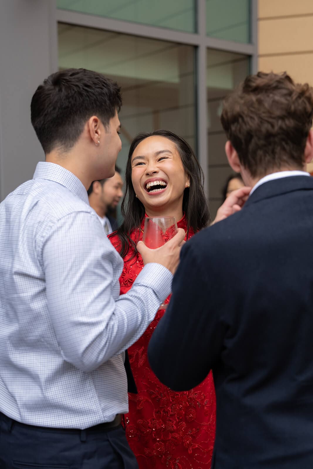 Woman in a red embroidered dress laughing while talking with guests and holding a drink.