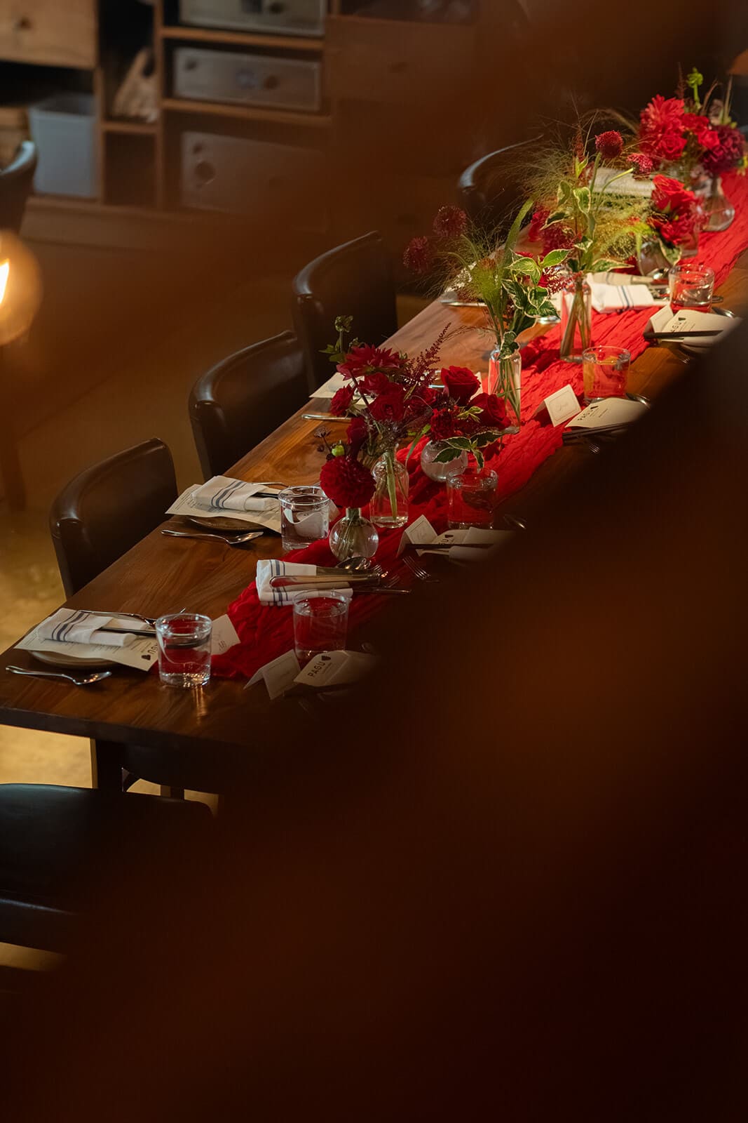 Long reception table glowing in warm evening light and decorated with red flowers for a pagu restaurant wedding dinner.