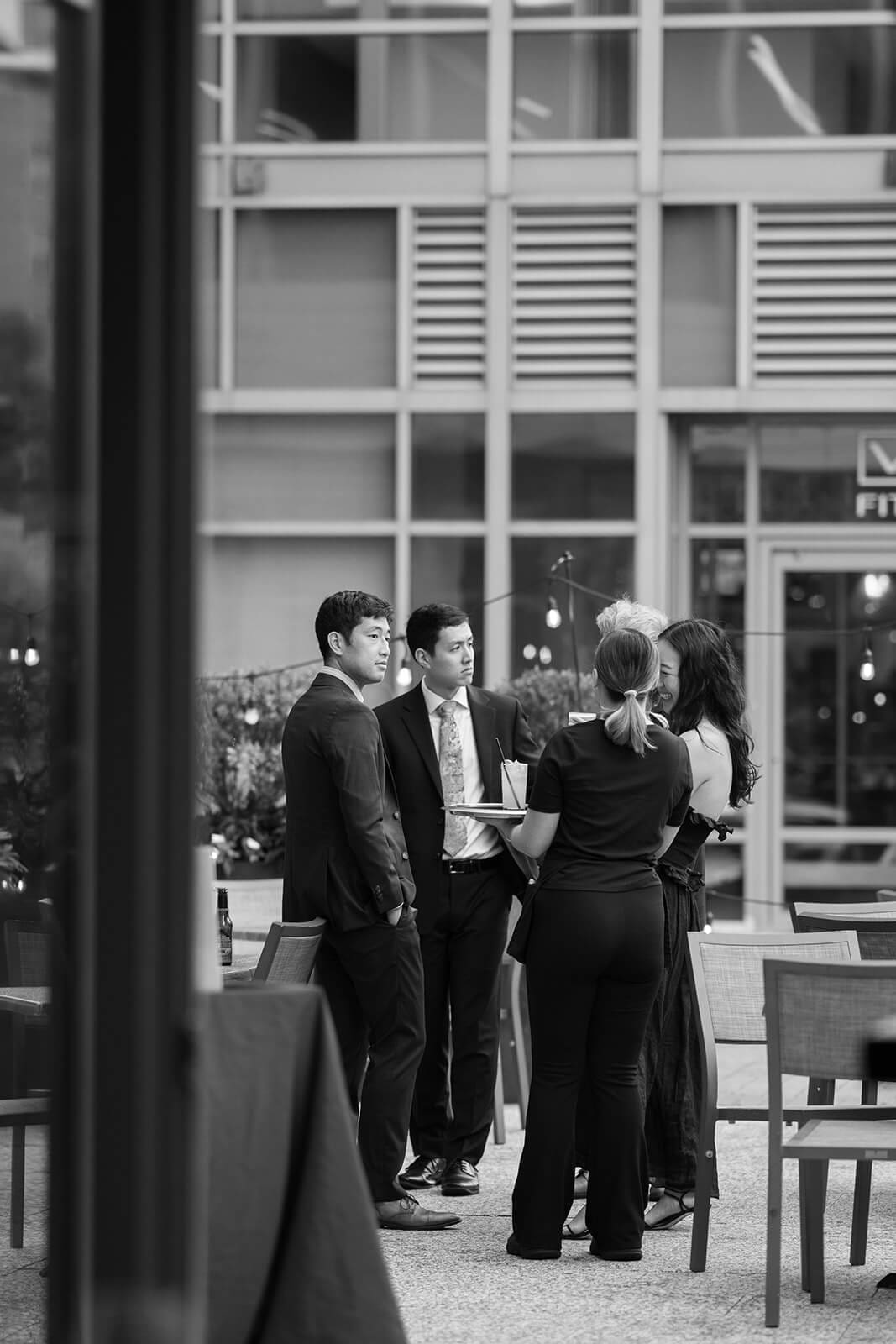Black-and-white candid of wedding guests talking together on an outdoor patio during a pagu restaurant wedding.