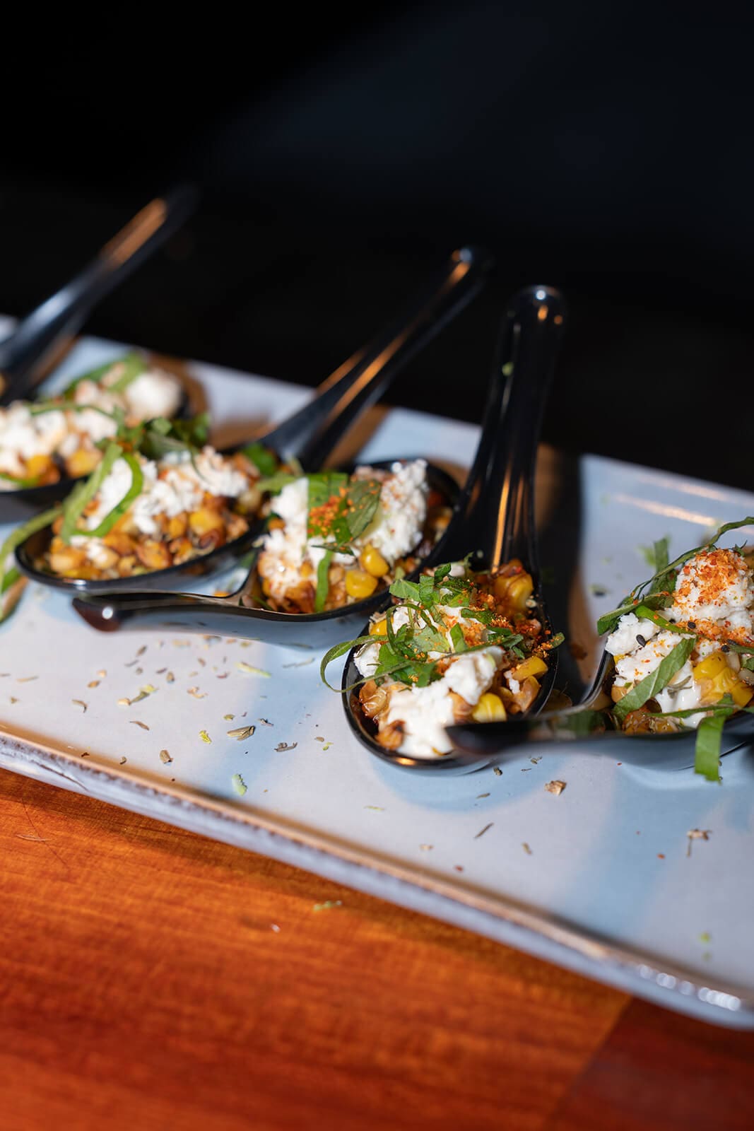 Individual appetizer portions topped with vegetables, herbs, and creamy sauce on black serving spoons.