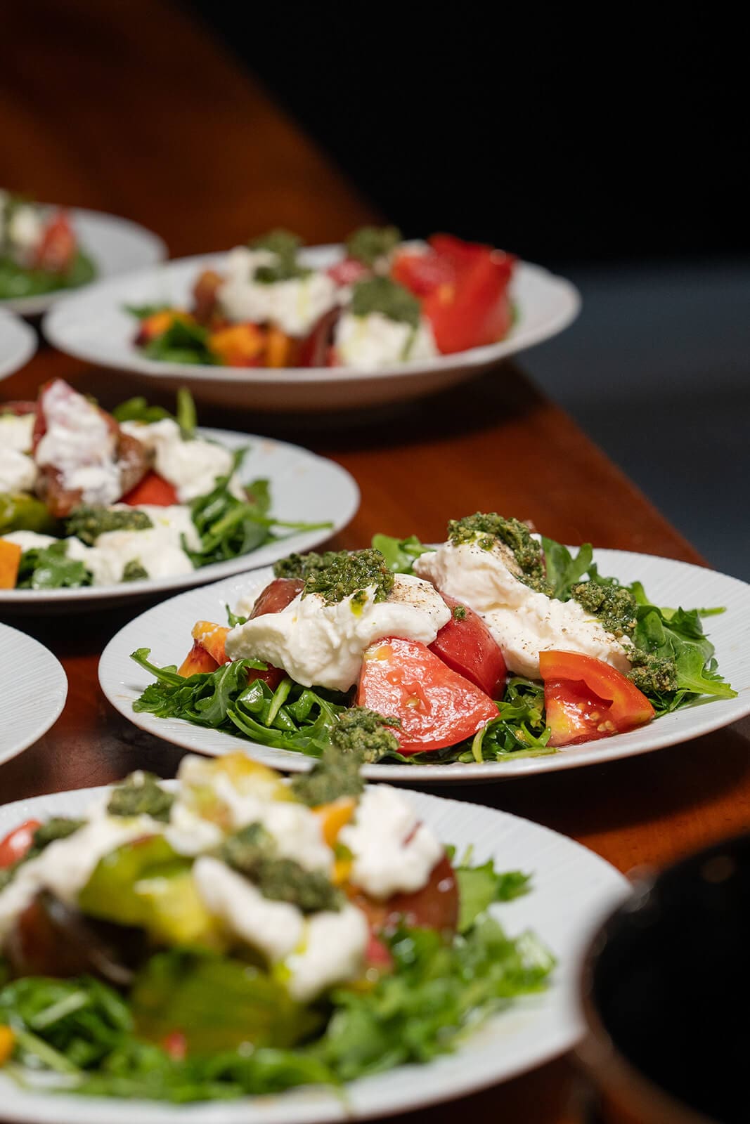 Plates of fresh tomato and greens topped with creamy cheese and herbs served at a pagu restaurant wedding dinner.