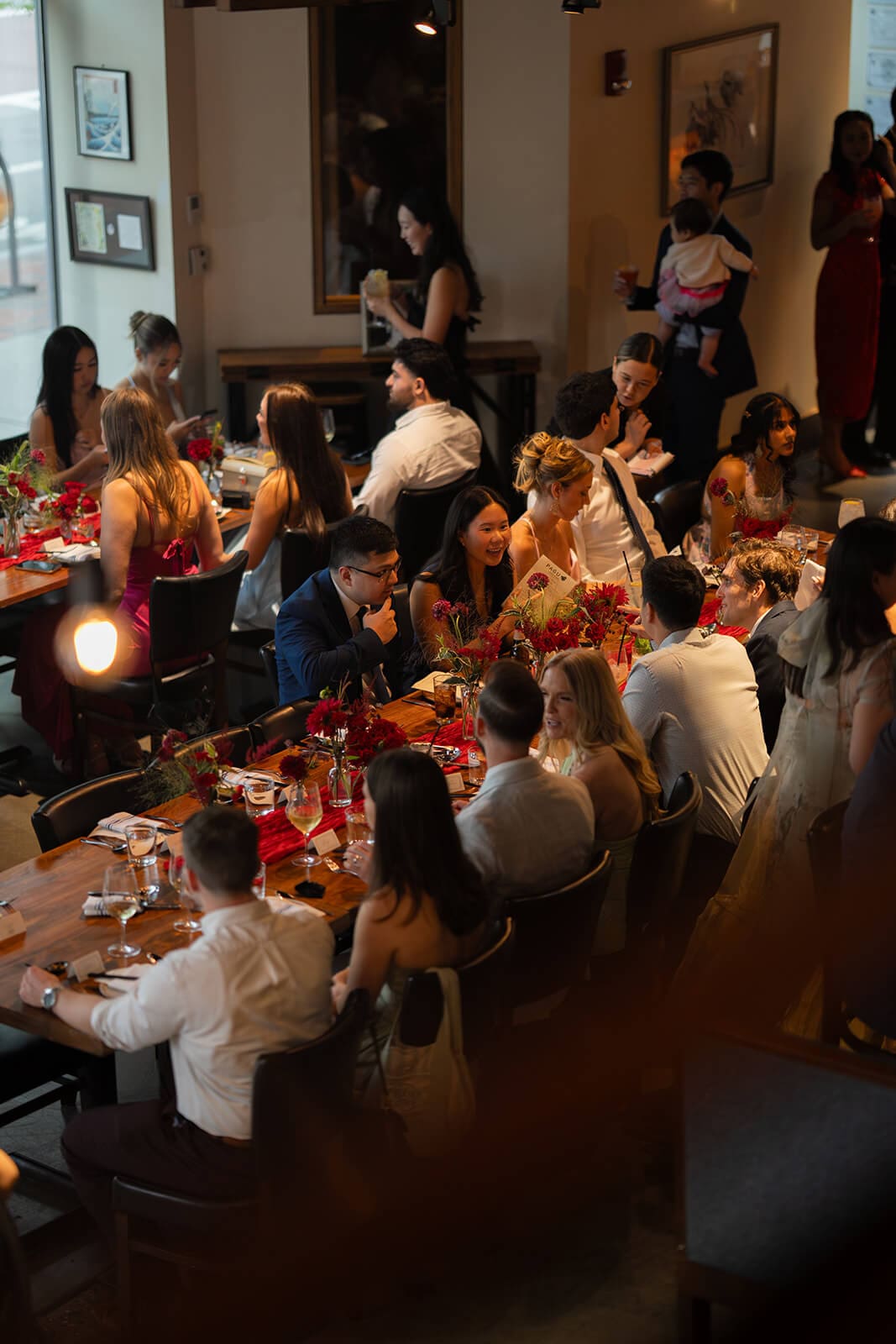 Overhead view of guests seated around a long, flower-filled table during a lively pagu restaurant wedding dinner.