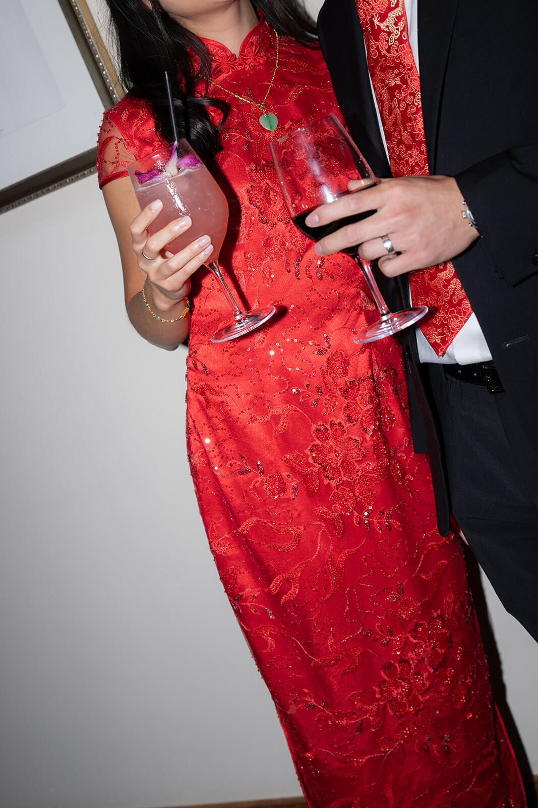 Close-up of the couple holding colorful drinks while dressed in red and black at their pagu restaurant wedding.