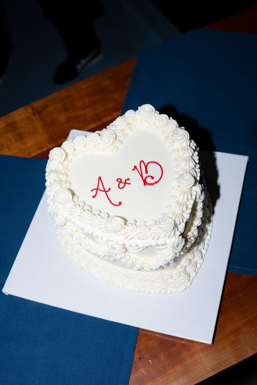 White heart-shaped vintage-style cake decorated with piped frosting and red initials on top.