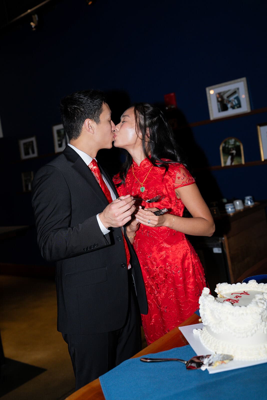 Couple kissing while holding pieces of cake after cutting their wedding cake.