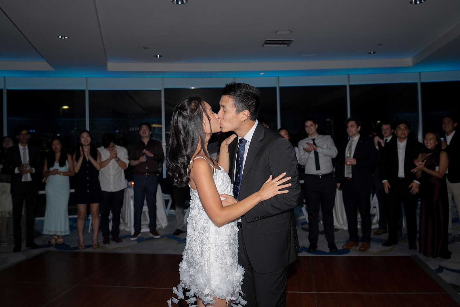 Newlyweds kissing on the dance floor while guests stand around them and applaud.