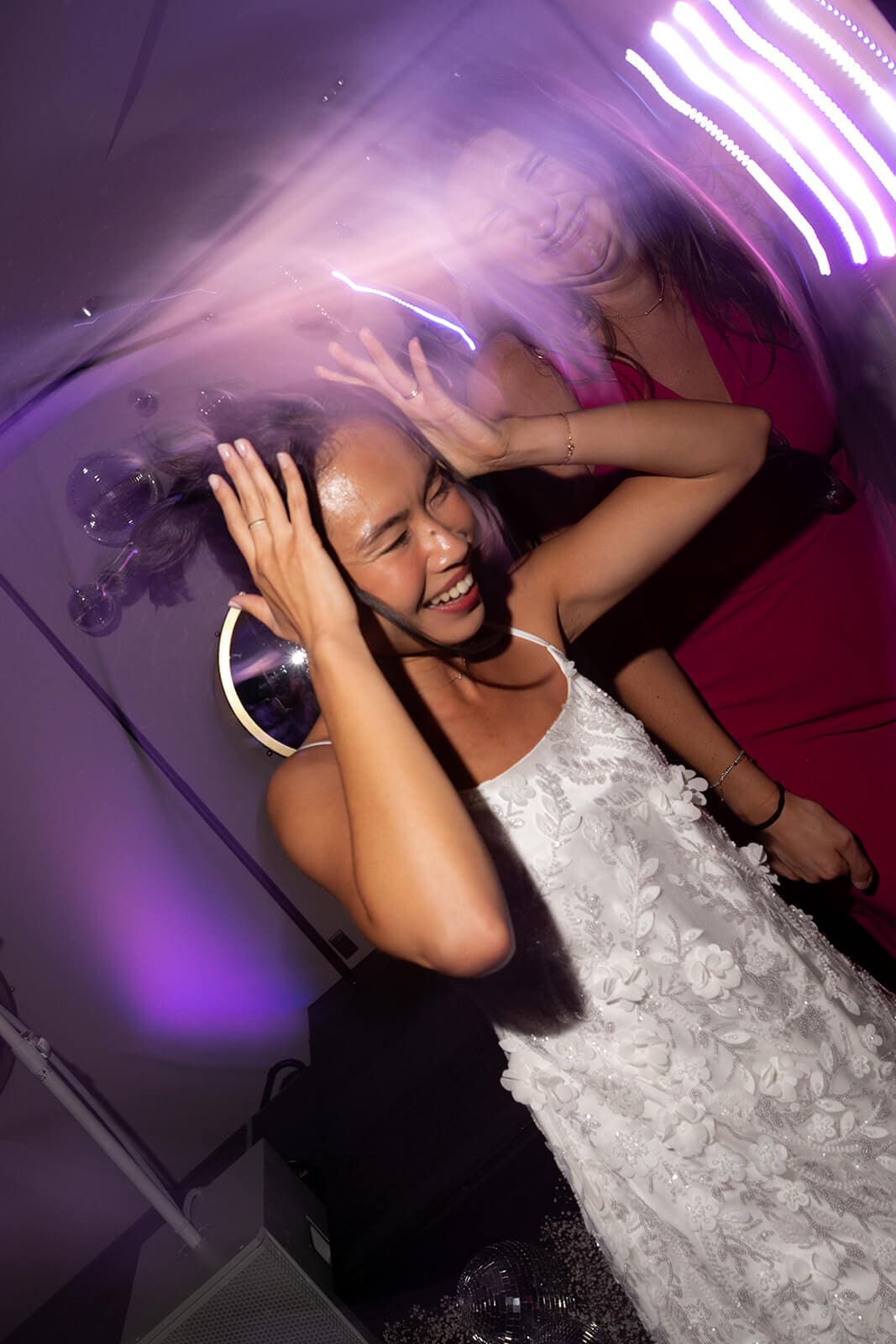Bride dancing beneath purple lights and laughing with friends during her pagu restaurant wedding reception.