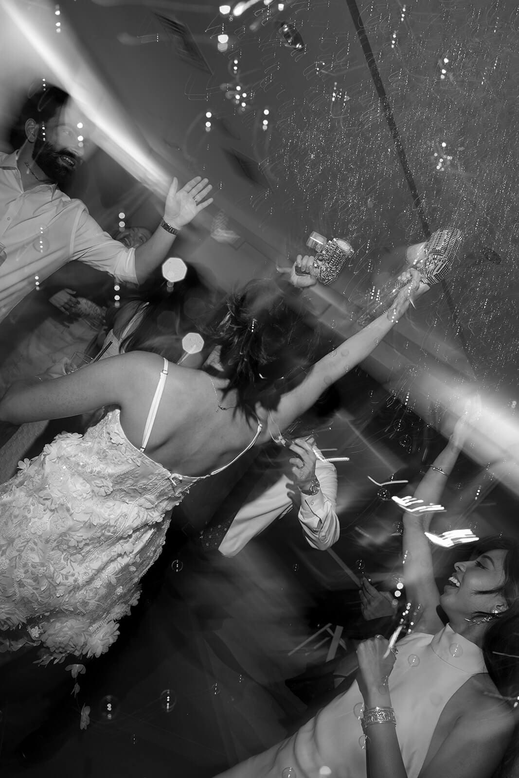Black-and-white overhead action shot of guests dancing and spraying bubbles during a lively pagu restaurant wedding reception.