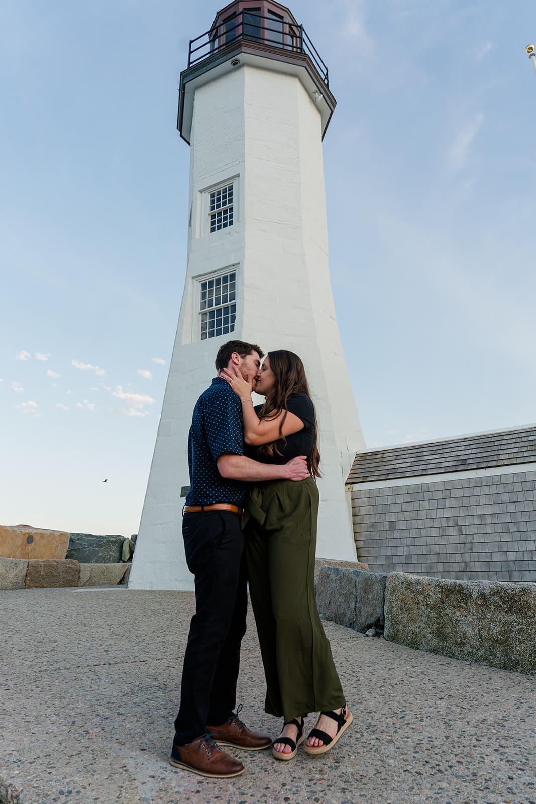 Engaged couple kissing in front of Scituate Lighthouse