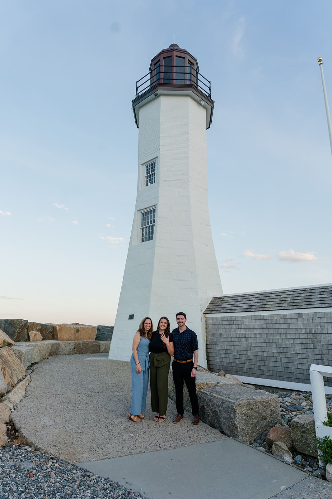 Newly engaged couple posing with a family member beside Scituate Lighthouse