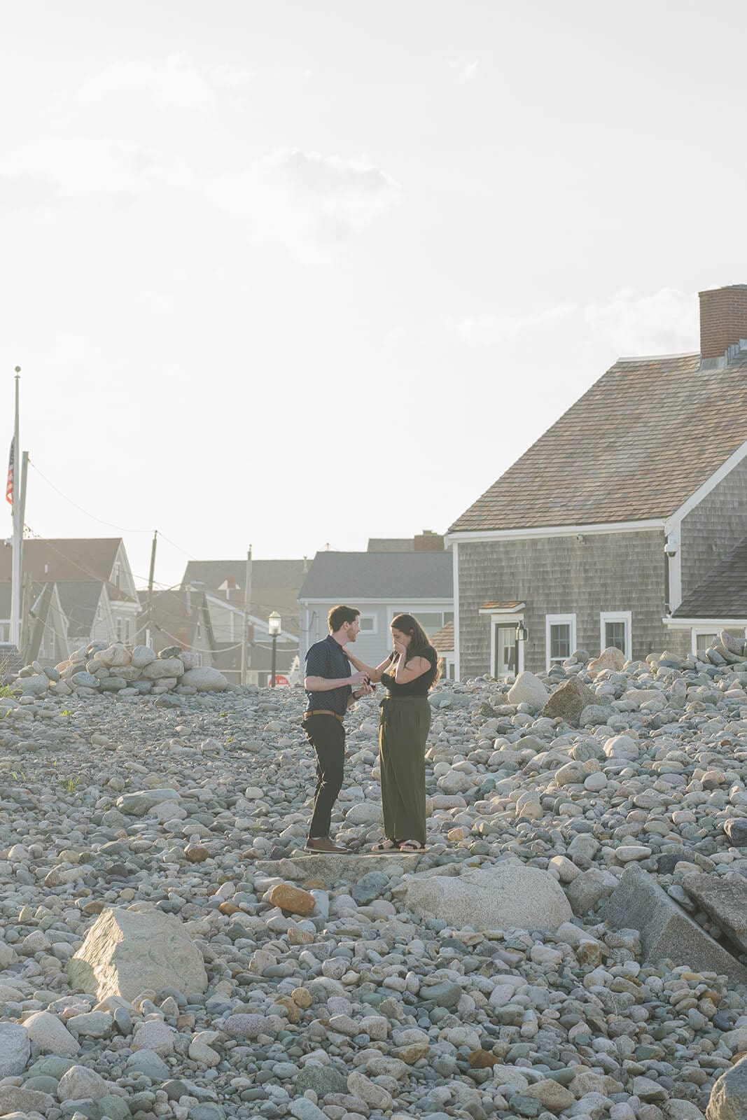 Couple standing together on the rocky shoreline with Scituate Lighthouse in the background