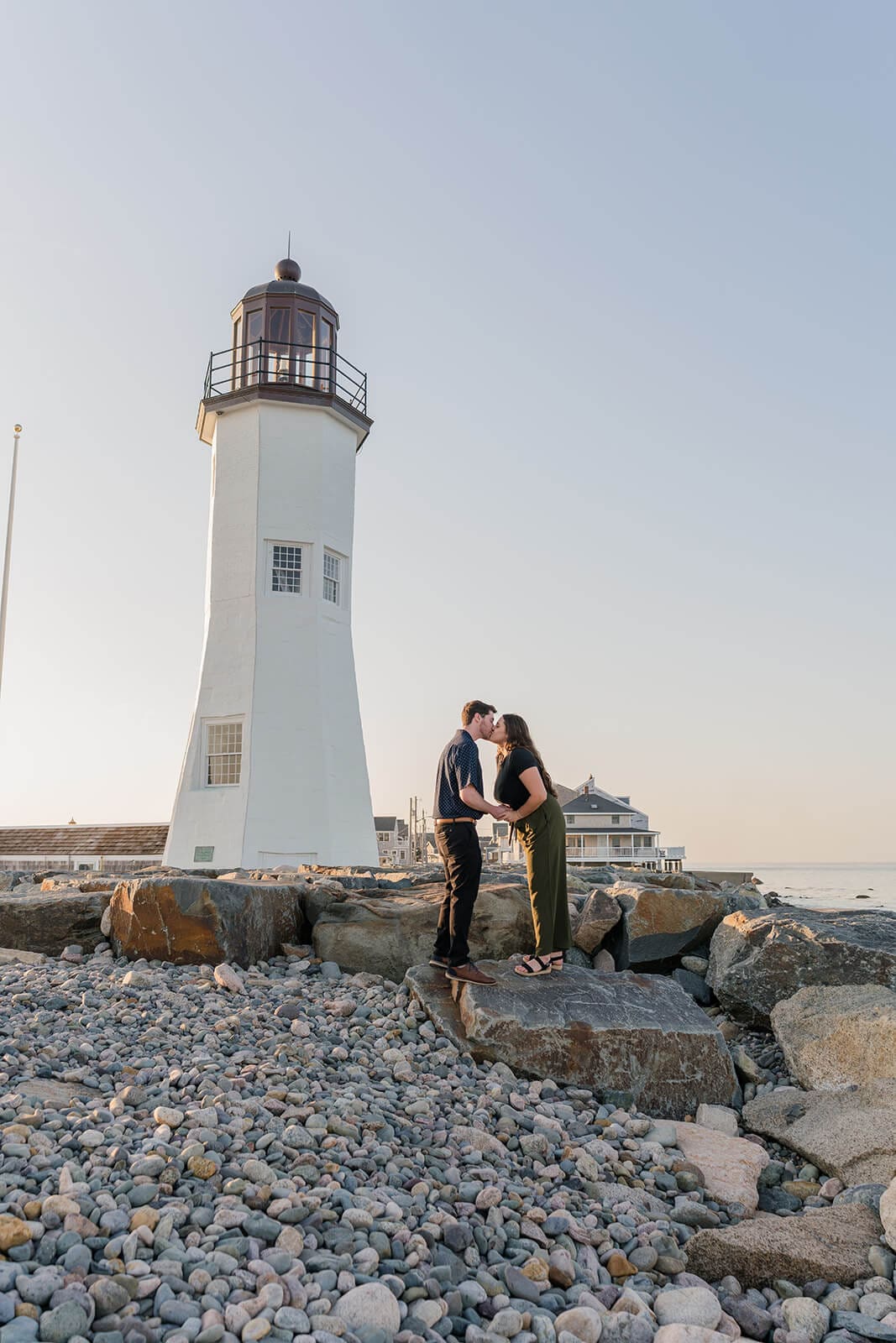 Couple standing together on the rocky shoreline with Scituate Lighthouse in the distance