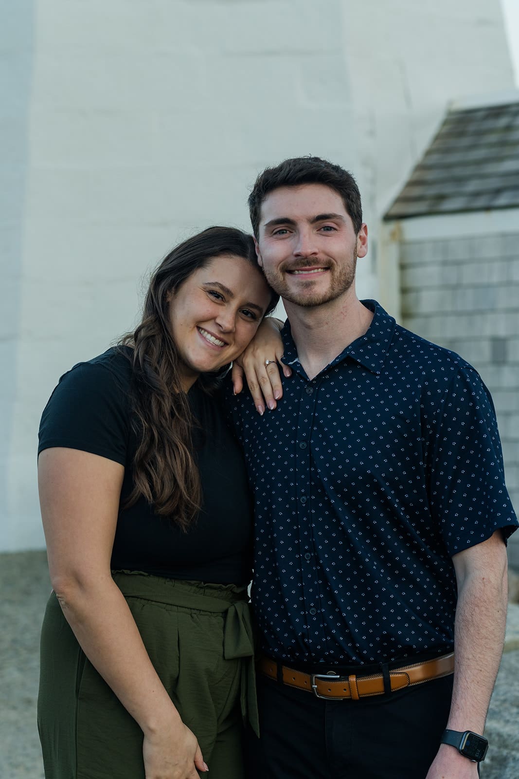 Newly engaged couple smiling together beside Scituate Lighthouse