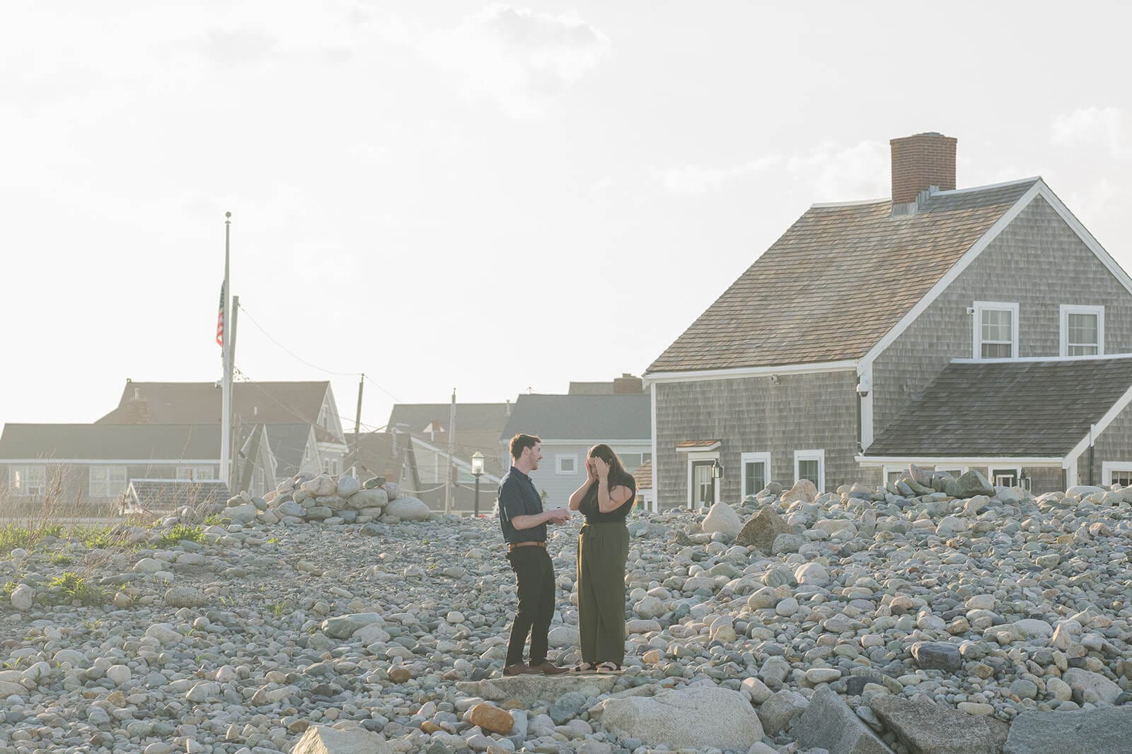 Couple standing together on the rocky shoreline near coastal buildings at Scituate Lighthouse