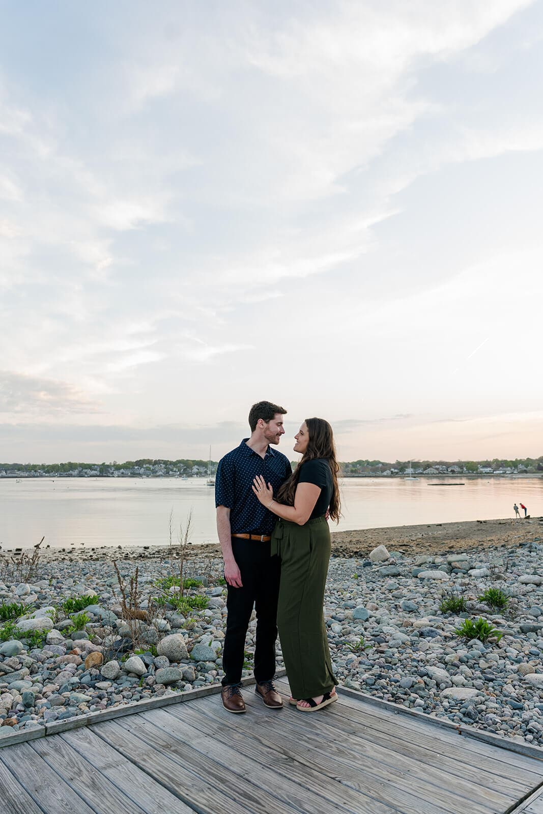 Newly engaged couple standing together on a waterfront boardwalk at sunset