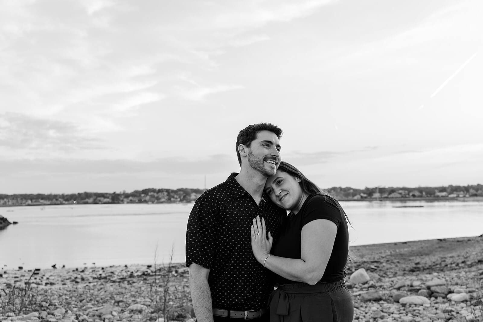 Black-and-white portrait of an engaged couple embracing along the rocky Scituate coastline