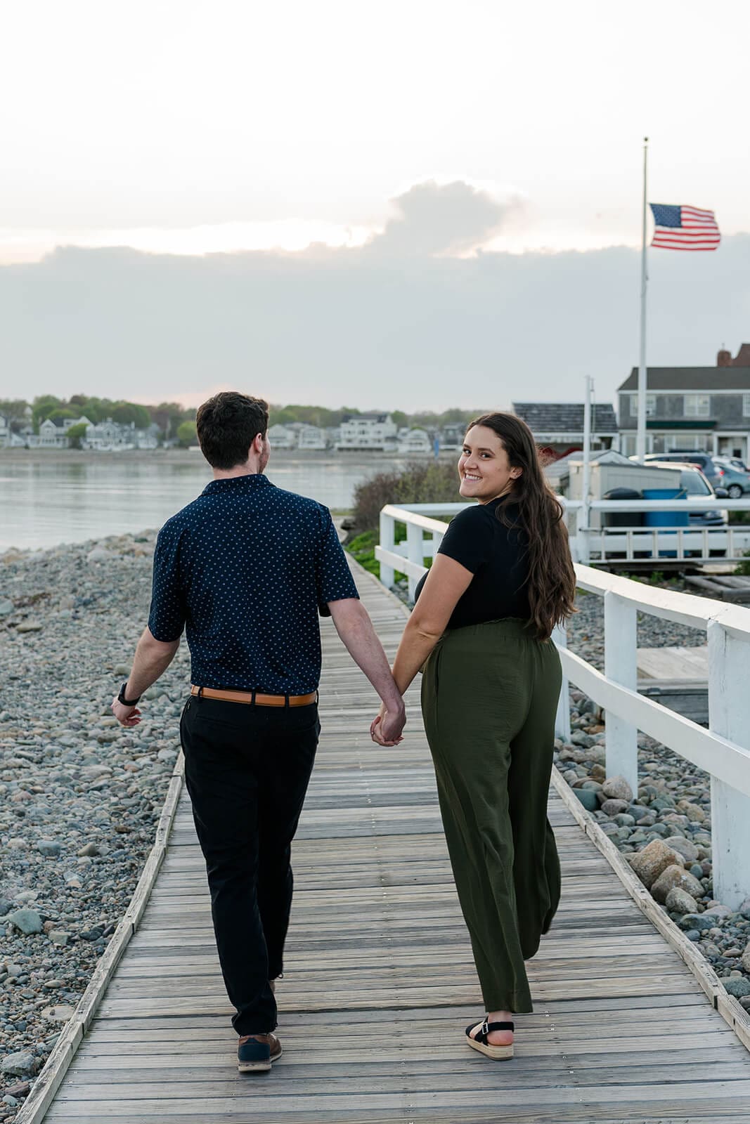 Engaged couple walking hand in hand along the boardwalk beside the harbor