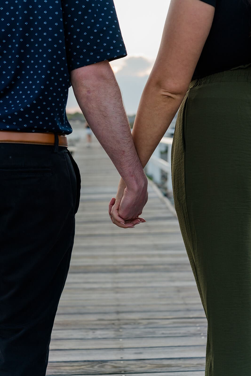 Close-up of an engaged couple holding hands while walking along a wooden boardwalk