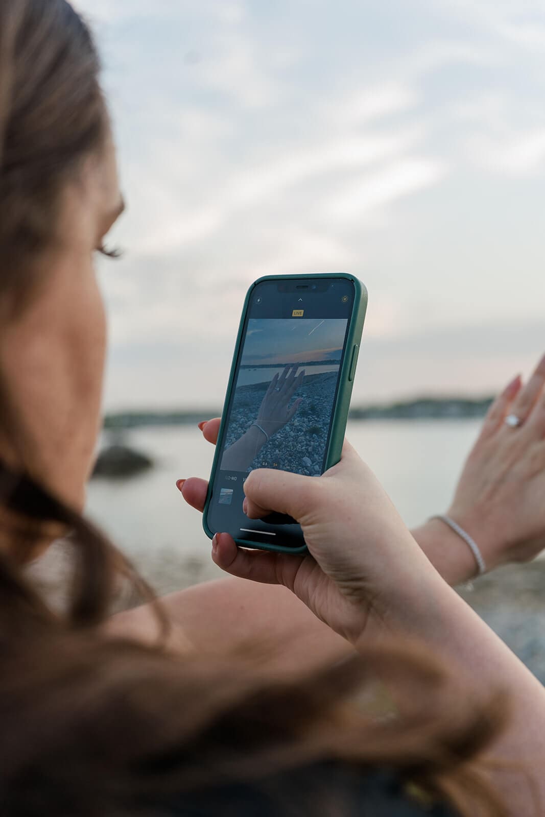 Close-up of a woman holding a phone while standing near the waterfront after a surprise proposal