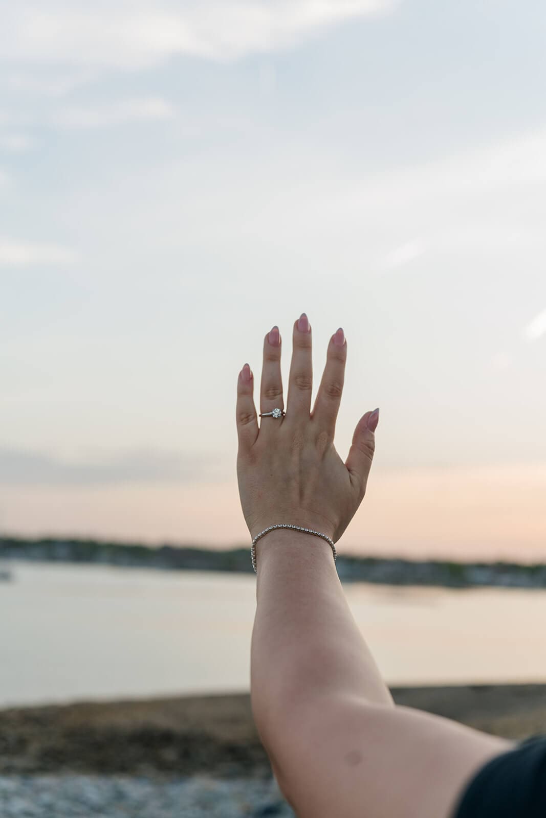 Woman holding her hand up to show her engagement ring against the sunset sky