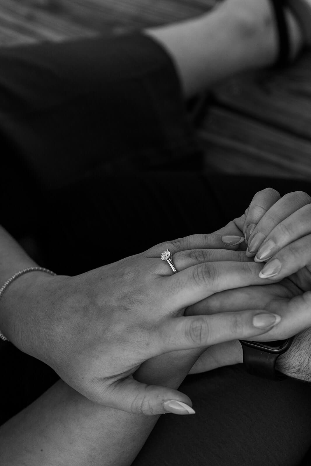Black-and-white close-up of a woman’s engagement ring resting on her partner’s hand