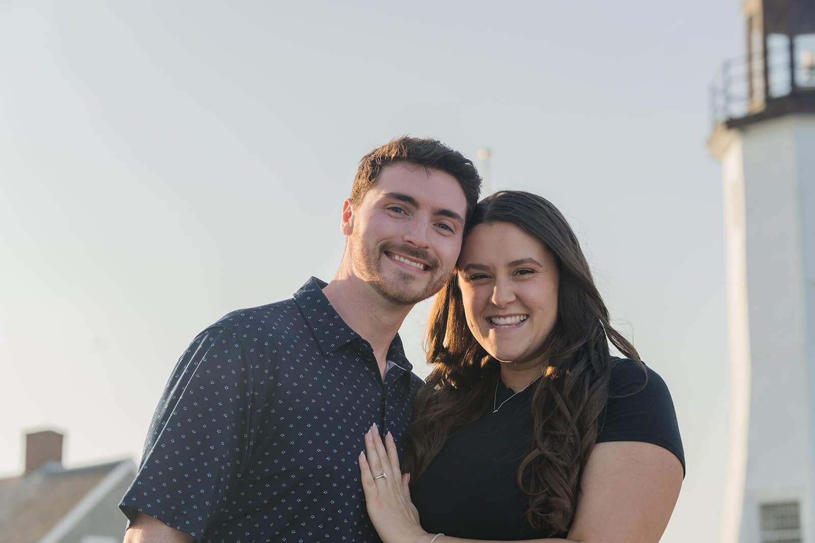 Newly engaged couple smiling together with Scituate Lighthouse behind them